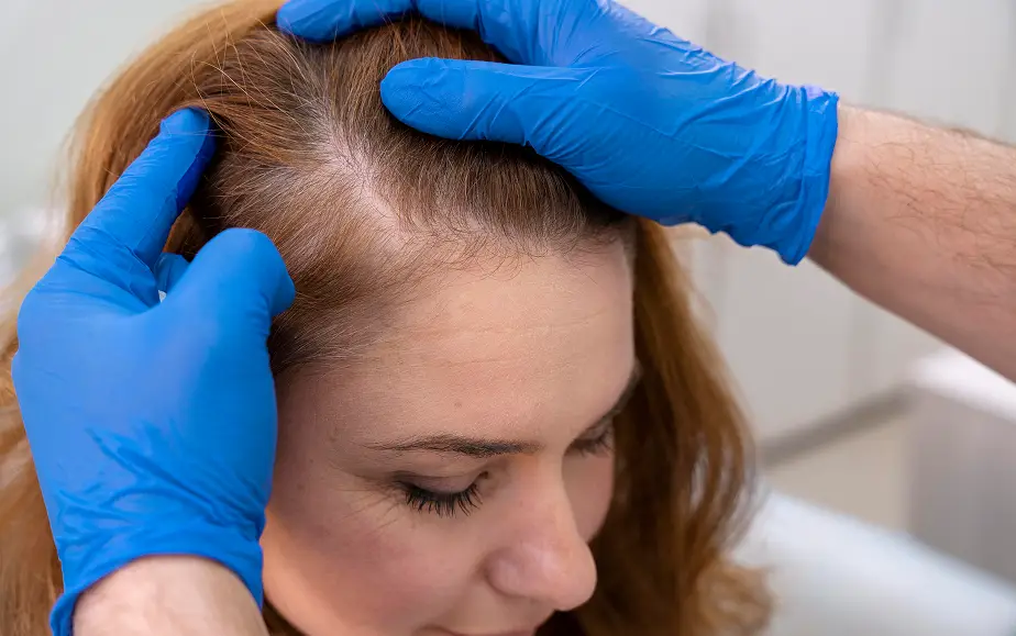 A professional examines a client’s scalp for a customized hair system solution.